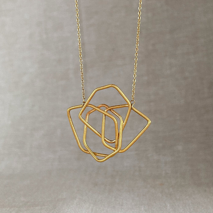 Das Collier Triade“ vereint unregelmäßig geformte, ineinander verschlungene Elemente zu einem harmonischen Mittelpunkt. Die klaren Linien und die sanft matte Oberfläche verleihen dem Schmuckstück eine ruhige, zugleich kraftvolle Ausstrahlung.