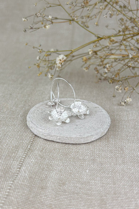 Zart und verspielt – die „Mini-Jacintos“ sind handgefertigte Ohrringe mit einer einzelnen, fein ziselierten Blüte, die sanft an einer Creole schwingt. Ihre schlichte Eleganz macht sie zu einem dezenten, aber besonderen Begleiter für jeden Tag.