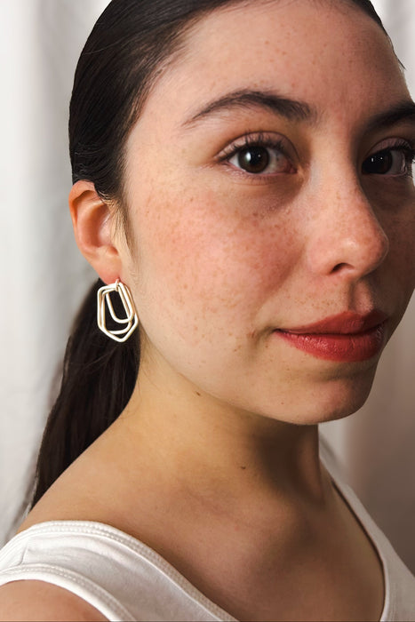 Zeitlos modern und doch handwerklich geprägt – diese geometrischen Ohrringe vereinen klare Linien mit warmer, goldener Ausstrahlung. Die ineinander verschlungenen Formen erzeugen Bewegung und Tiefe, während die matte Oberfläche einen sanften Glanz verleiht.