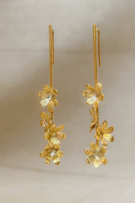 Die Ohrringe „Jacintos“ verbinden schlichte Eleganz mit handwerklicher Präzision. Mehrere kleine, von Hand geformte Blüten hängen aneinander und erzeugen bei jeder Bewegung ein feines Spiel aus Glanz und Struktur.