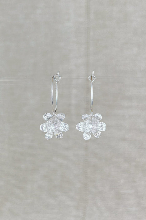 Zart und verspielt – die „Mini-Jacintos“ sind handgefertigte Ohrringe mit einer einzelnen, fein ziselierten Blüte, die sanft an einer Creole schwingt. Ihre schlichte Eleganz macht sie zu einem dezenten, aber besonderen Begleiter für jeden Tag.