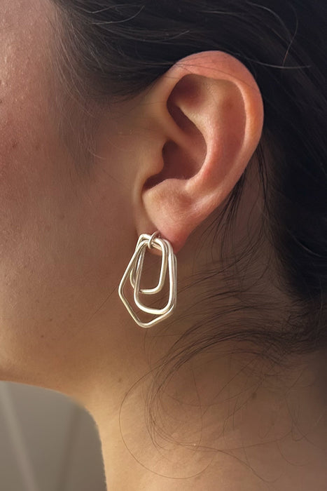 Zeitlos modern und doch handwerklich geprägt – diese geometrischen Ohrringe vereinen klare Linien mit warmer, goldener Ausstrahlung. Die ineinander verschlungenen Formen erzeugen Bewegung und Tiefe, während die matte Oberfläche einen sanften Glanz verleiht.