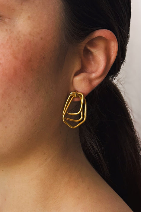 Zeitlos modern und doch handwerklich geprägt – diese geometrischen Ohrringe vereinen klare Linien mit warmer, goldener Ausstrahlung. Die ineinander verschlungenen Formen erzeugen Bewegung und Tiefe, während die matte Oberfläche einen sanften Glanz verleiht.