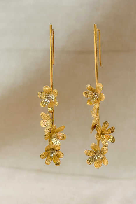 Die Ohrringe „Jacintos“ verbinden schlichte Eleganz mit handwerklicher Präzision. Mehrere kleine, von Hand geformte Blüten hängen aneinander und erzeugen bei jeder Bewegung ein feines Spiel aus Glanz und Struktur.