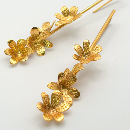 Die Ohrringe „Jacintos“ verbinden schlichte Eleganz mit handwerklicher Präzision. Mehrere kleine, von Hand geformte Blüten hängen aneinander und erzeugen bei jeder Bewegung ein feines Spiel aus Glanz und Struktur.